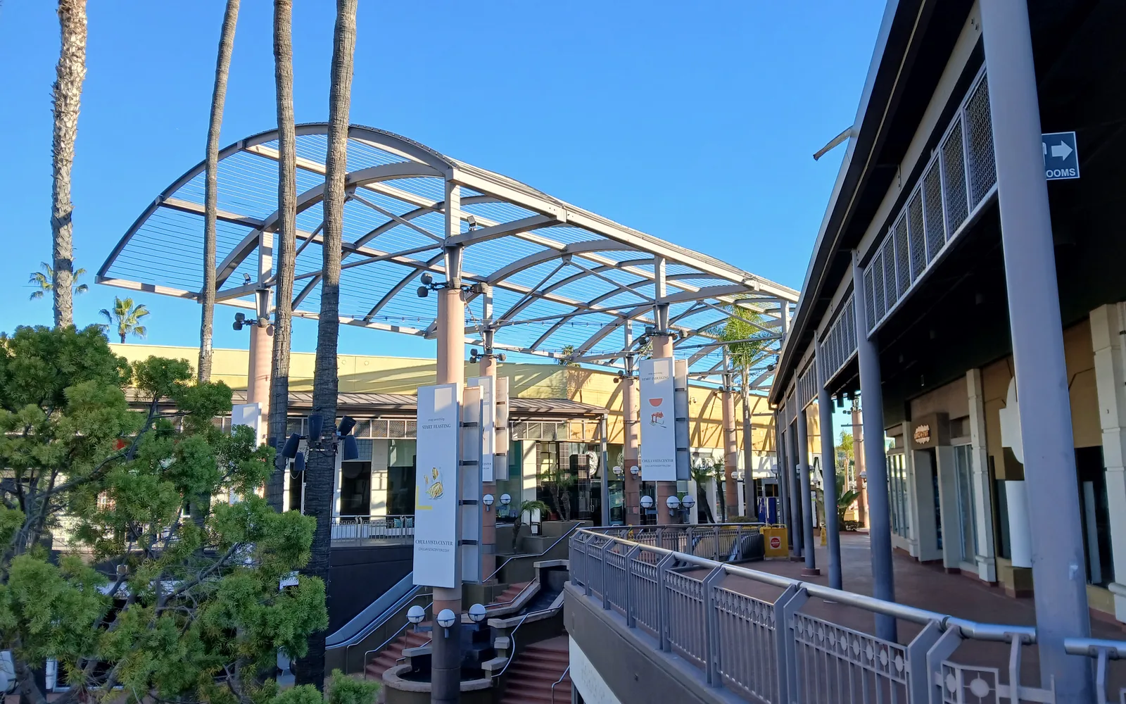 Outdoor shopping center with modern storefront architecture, wide plaza area, and multiple retail spaces in daylight